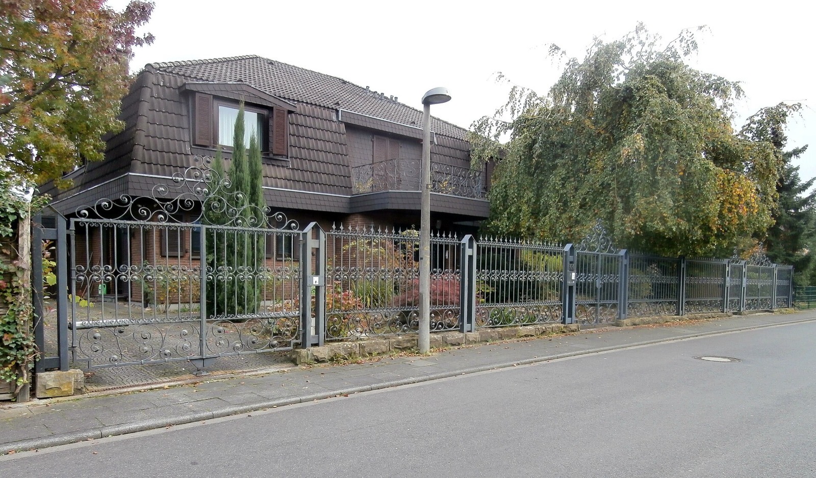 Wohnhaus an der Straße Am Waldpark in Köln-Hahnwald hinter einem schmiedeeisernen Zaun, umgeben von altem Baumbestand
