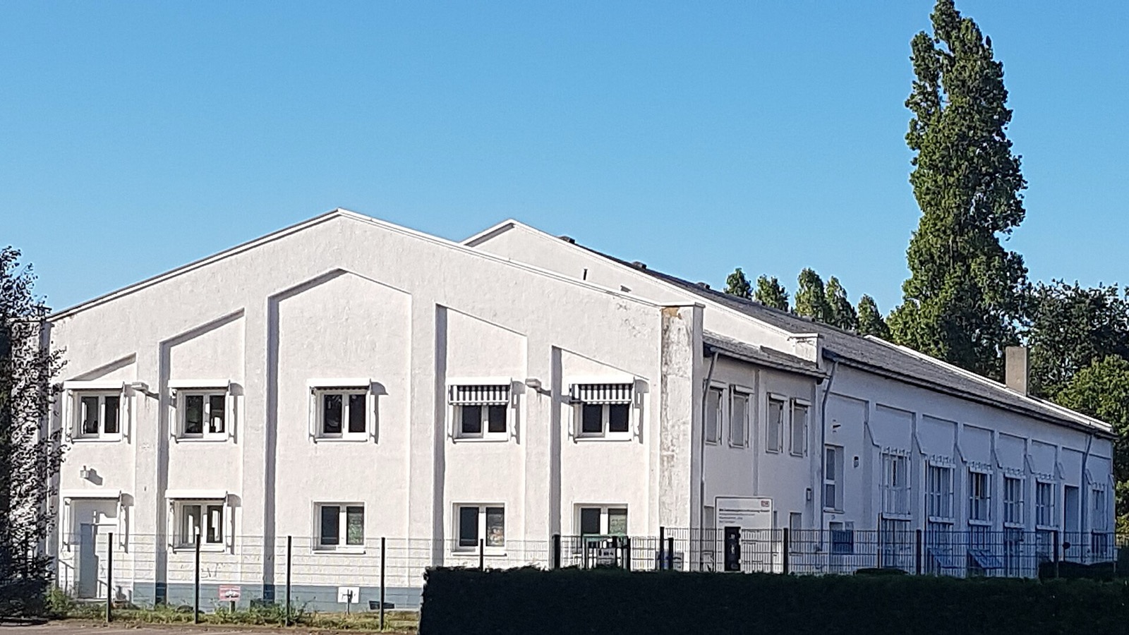 Weiß verputzter Hallenbau an der Werkstattstraße 100 in Köln-Nippes vor blauem Himmel