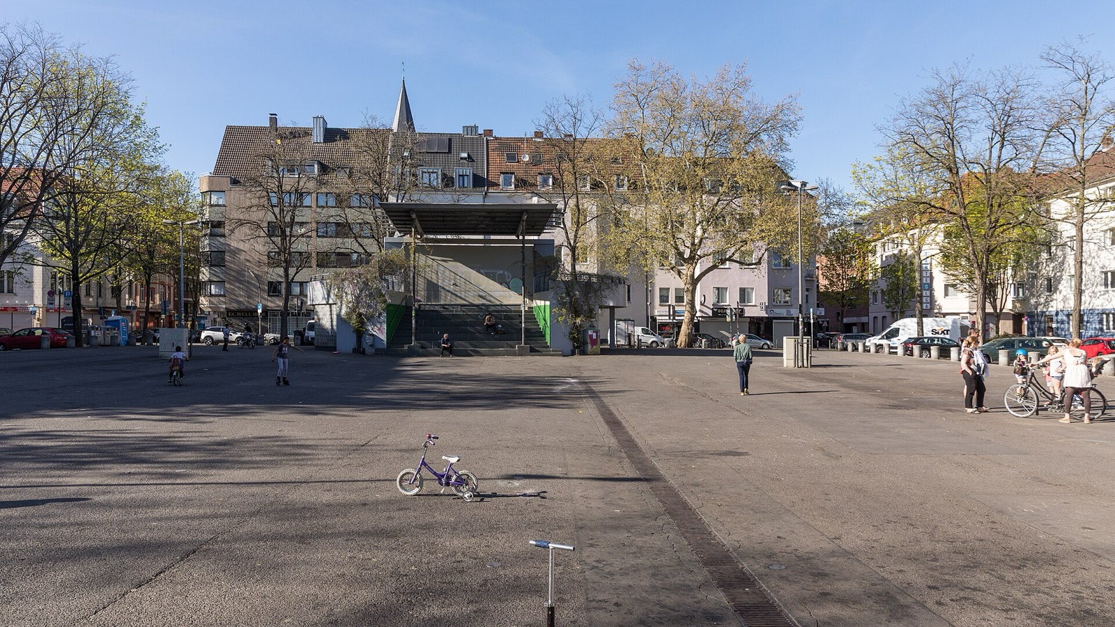Der Wilhelmplatz in Köln-Nippes ohne Markt: weite gepflasterte Fläche, umgeben von Wohn- und Geschäftshäusern