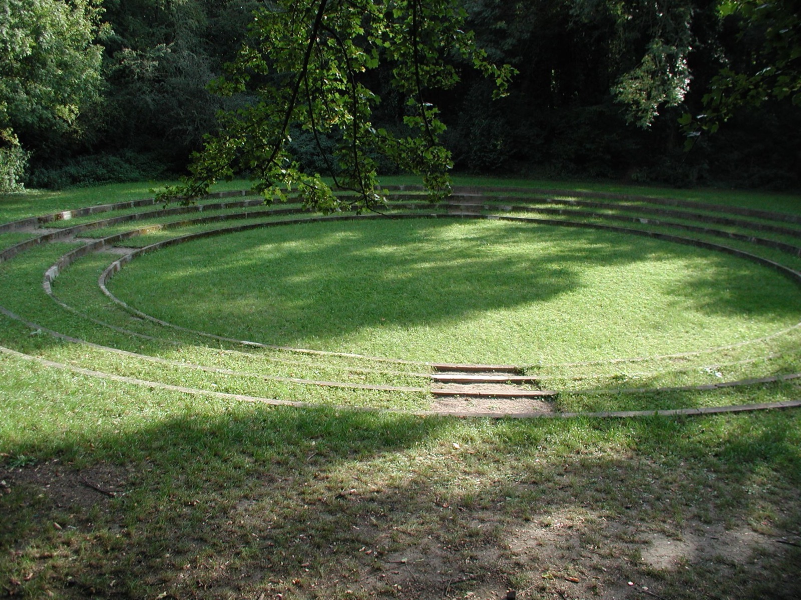 Das Naturtheater im Fritz-Encke-Volkspark in Köln-Raderthal: eine kreisrunde Rasenfläche mit umlaufenden Sitzstufen unter altem Baumbestand