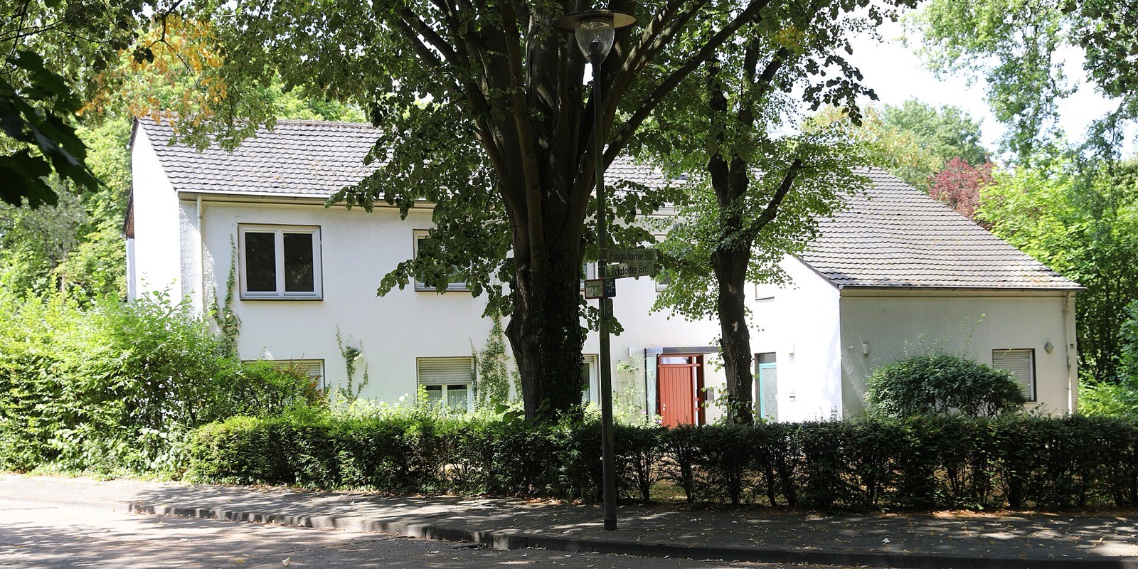 Weiß verputztes Wohnhaus an der Ecke Pingsdorfer Straße und Eckdorfer Straße in Köln-Raderthal, umgeben von altem Baumbestand und Hecken