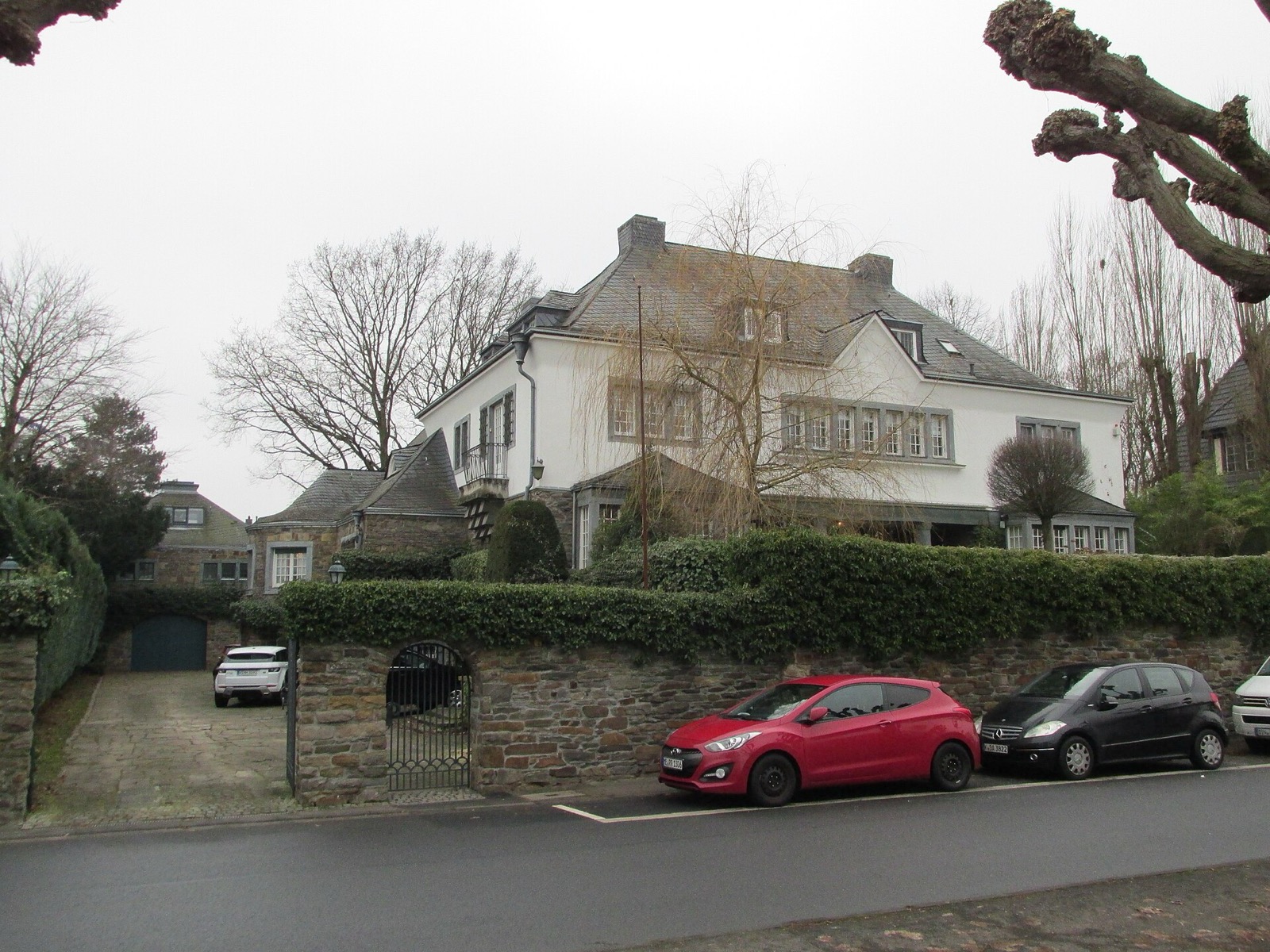 Großes weiß verputztes Landhaus mit Schieferdach hinter einer Bruchsteinmauer und Hecke an der Uferstraße in Köln-Rodenkirchen
