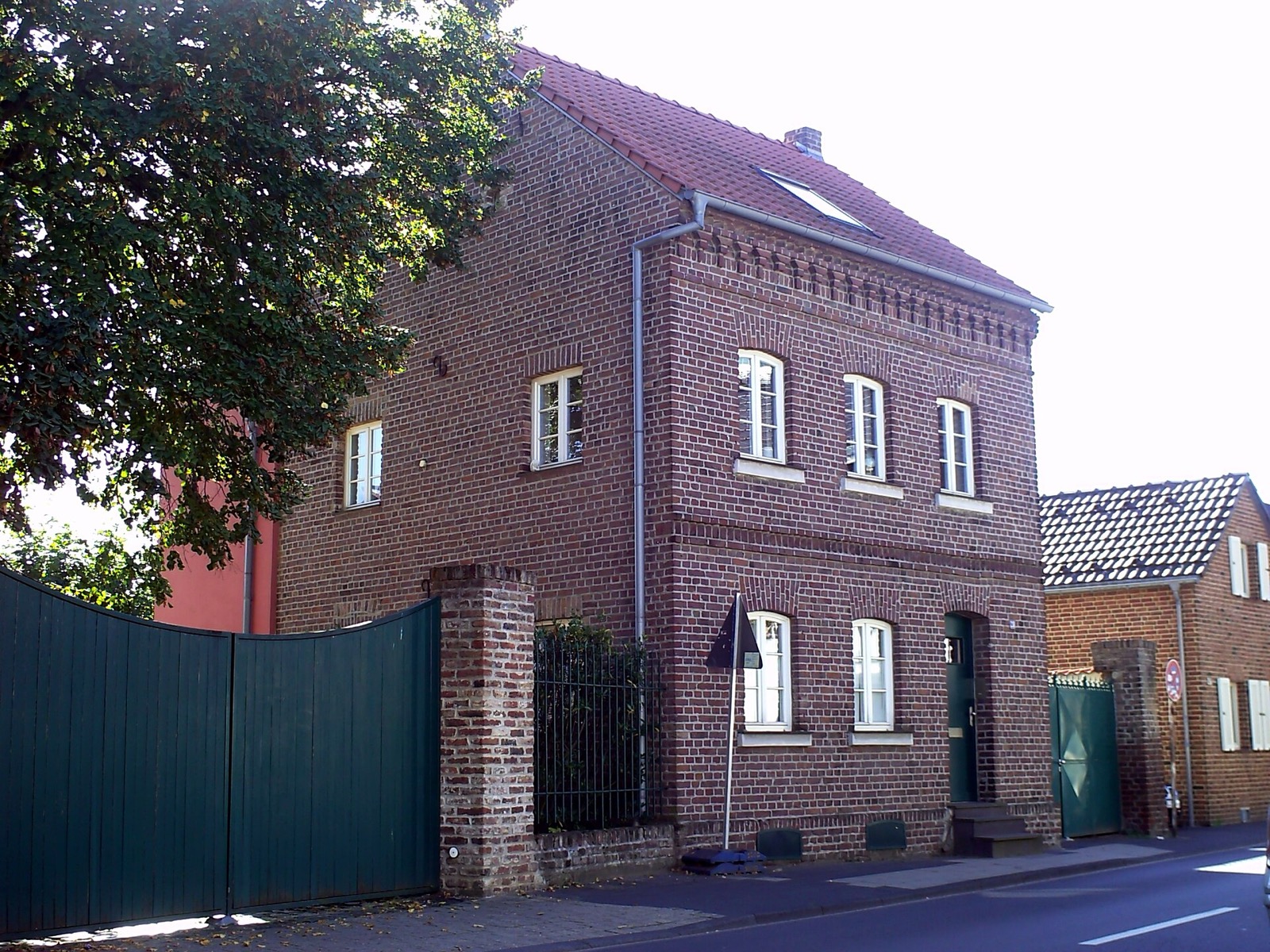 Denkmalgeschütztes Backsteinhaus an der Sürther Hauptstraße 28 mit Ziegeldach und grünem Hoftor