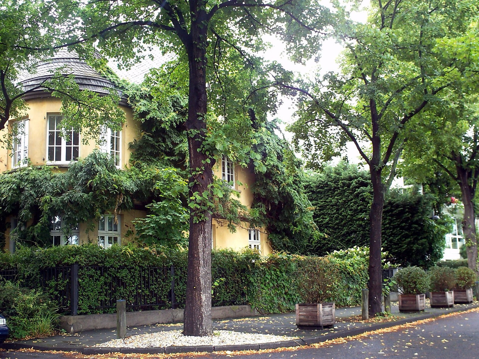 Villa mit rundem Eckturm und ockerfarbener Fassade hinter altem Baumbestand an der Carl-von-Linde-Straße in Köln-Sürth